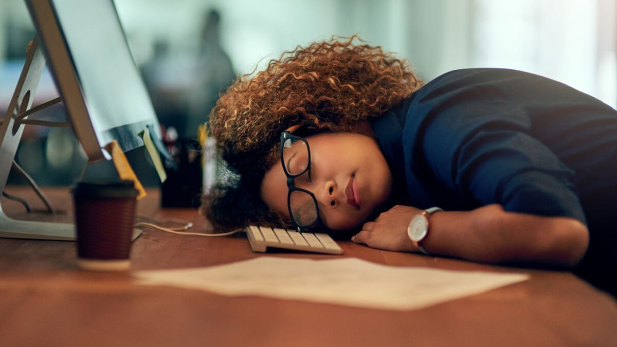 mulher dormindo em sua mesa do trabalho, com óculos tortos